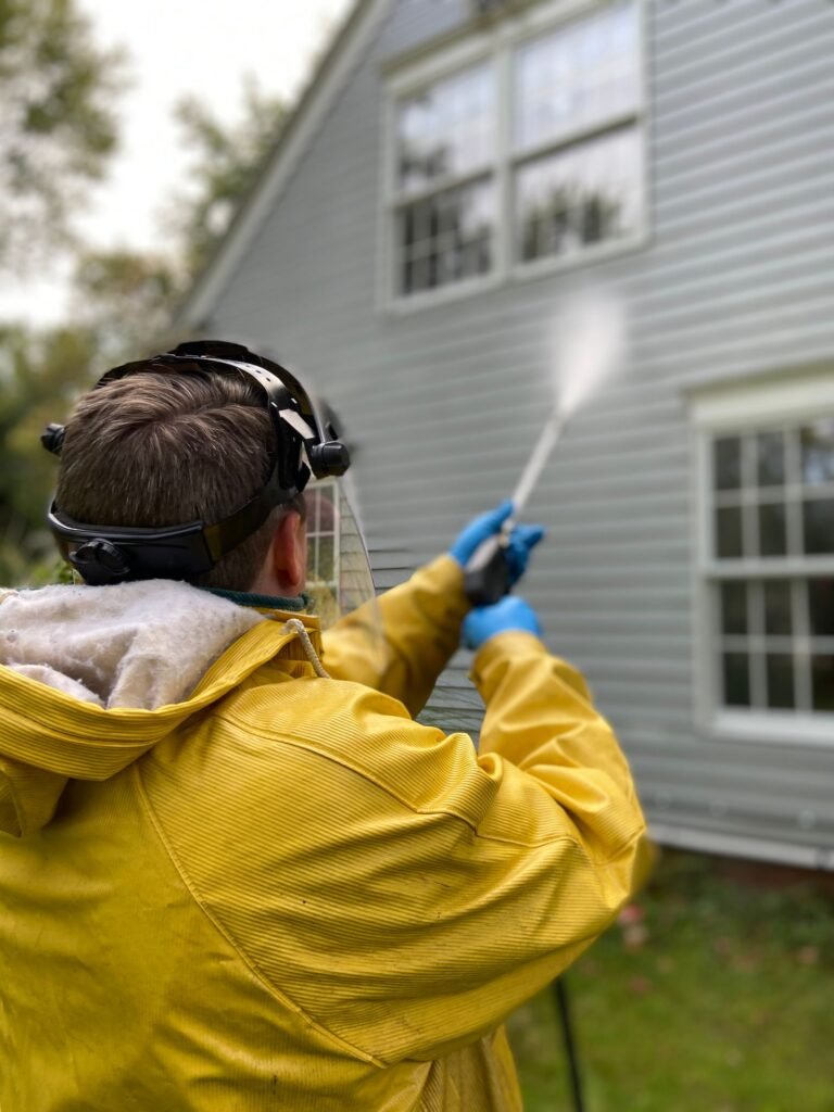 Worker washing house siding with a spray wand